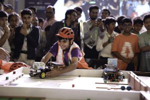 Noi amb casc participant en un repte de robòtica, preparant un robot mentre el públic observa.