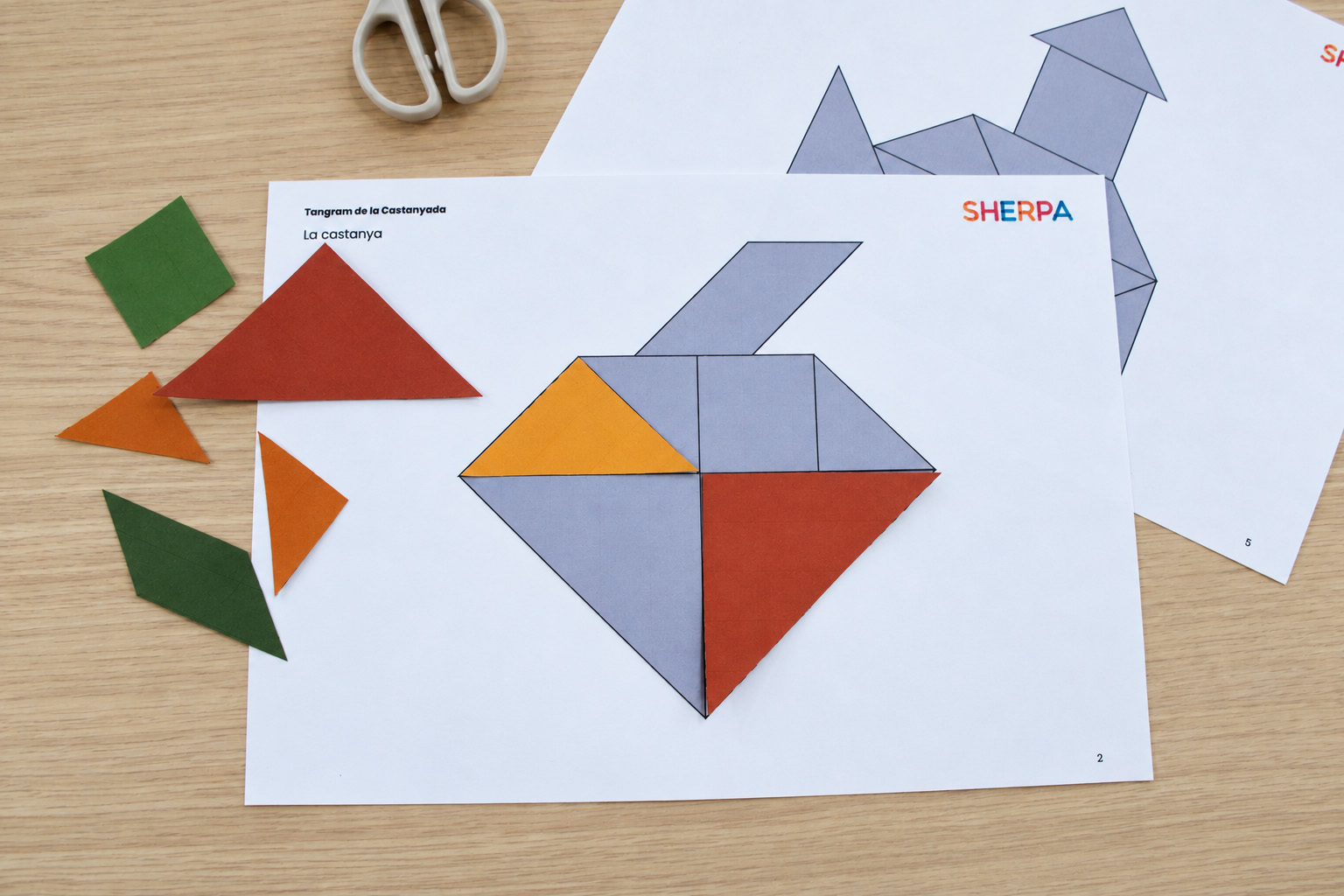 Activitat del tangram de la Castanyada amb peces de paper de colors i un full de treball amb la figura d'una castanya