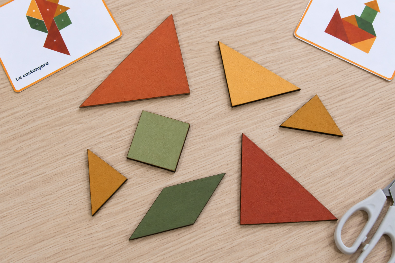Set peces geomètriques de fusta del tangram pintades amb colors de tardor i distribuïdes sobre una taula